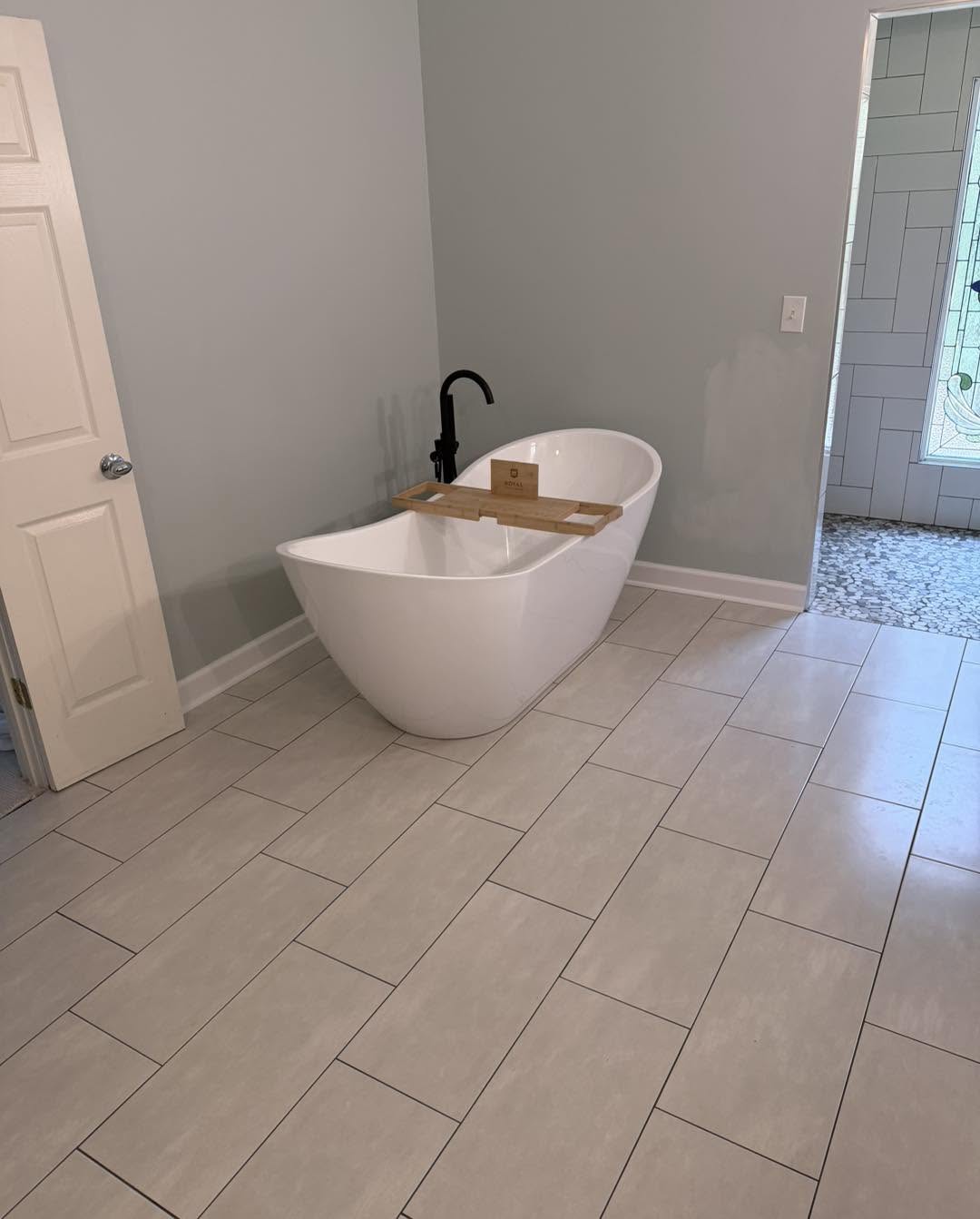 Freestanding soaking tub with bamboo tray on large-format tile by Fisher Remodeling