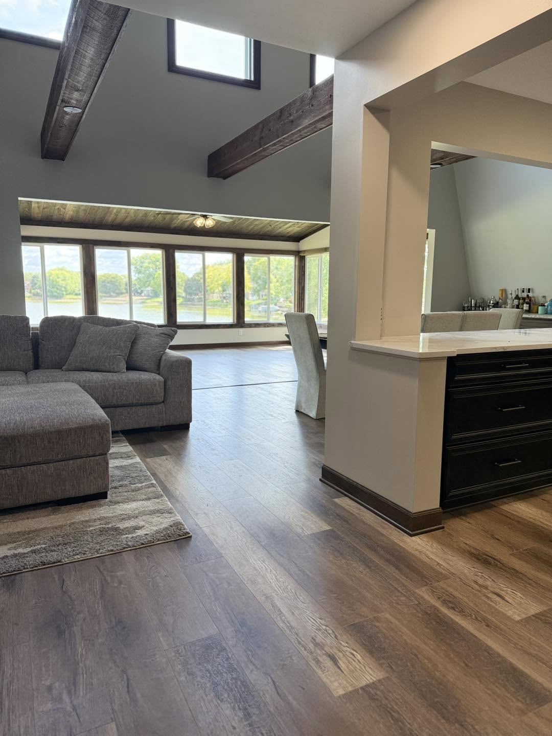 Vaulted living room with exposed wood beams and lake-view windows by Fisher Remodeling