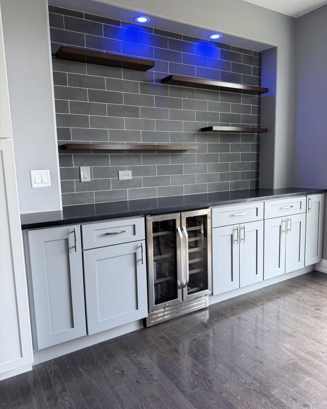 Basement wet bar with grey tile backsplash, floating shelves and wine fridge by Fisher Remodeling