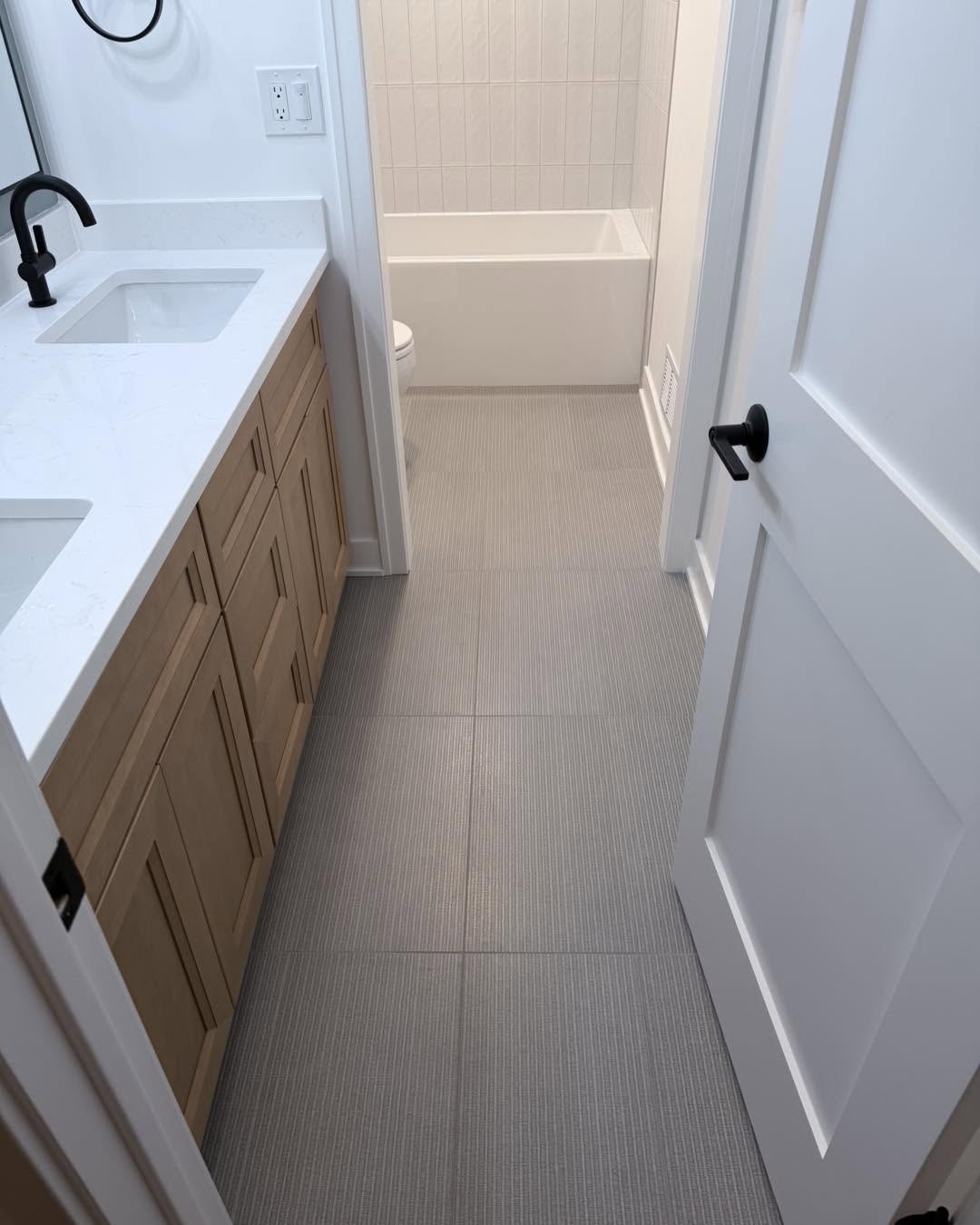 Hall bath vanity with new tile flooring and soaking tub beyond by Fisher Remodeling