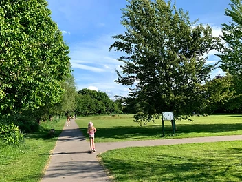 Navigation Park in Altrincham, with a paved path leading through green lawns and mature trees on a sunny afternoon.