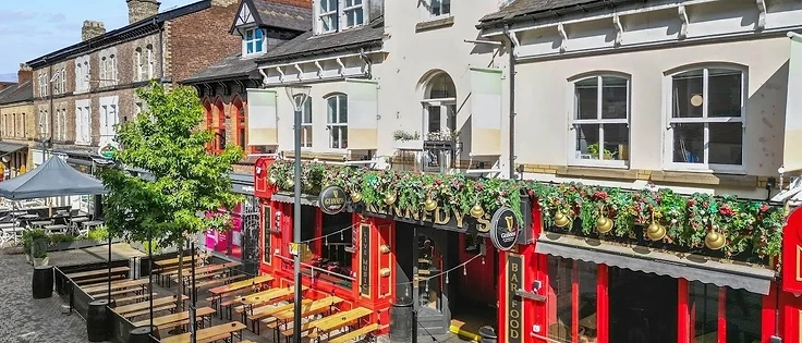 Exterior of Kennedy's Irish Bar in Altrincham with red facade, hanging baskets and outdoor seating
