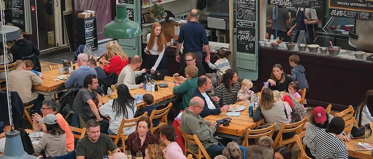 Busy Market House interior with communal dining tables and independent food stalls including Honest Crust pizza.