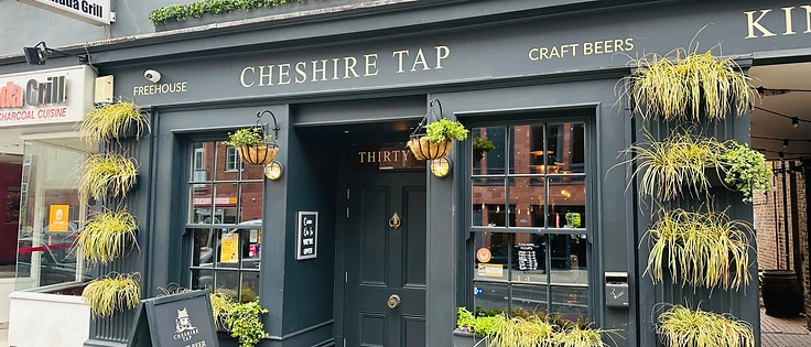 Exterior of Cheshire Tap freehouse in Altrincham, with hanging baskets and chalkboard sign