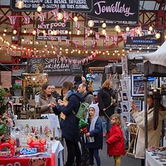 Crowds browsing the outdoor Altrincham Market stalls under string lights and Union Jack bunting.
