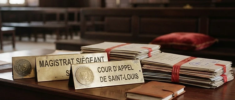 A close-up view of official judicial appointment files and brass nameplates resting on a courtroom bench at the Saint-Louis Court of Appeal in Senegal.