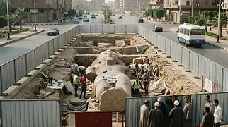 Cordoned-off archaeological excavation pits containing stone statue fragments are shown from an elevated perspective in Bahbit Al-Higara, Egypt.