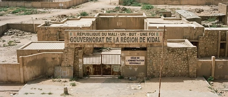 The derelict entrance plaque and faded administrative signs of the regional governor's office sit in a quiet, sun-bleached courtyard in Kidal.