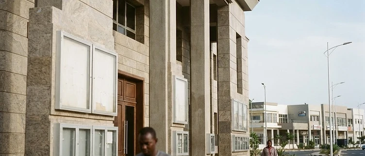 The imposing entrance of the Touba Municipal Council building stands under a bright sky with empty information boards displayed on its facade.