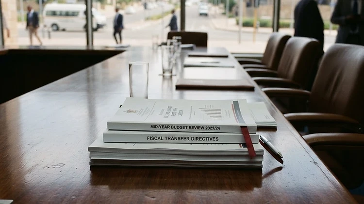 Official municipal budget review documents and central fiscal transfer directives are arranged on a wooden table inside the Windhoek City Council chamber.