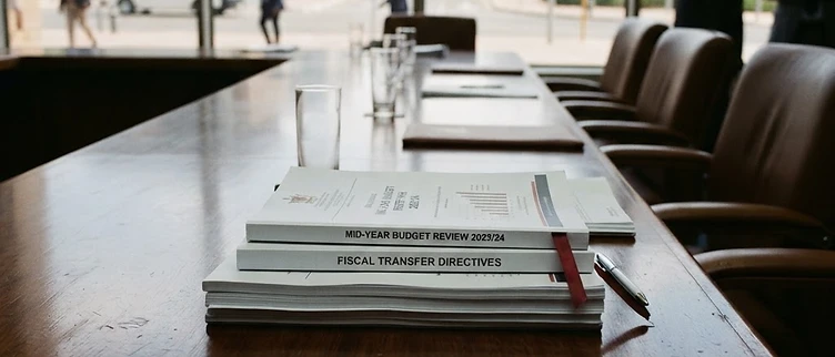 Official municipal budget review documents and central fiscal transfer directives are arranged on a wooden table inside the Windhoek City Council chamber.
