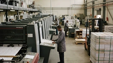 High-security industrial ballot printing presses and stacks of electoral paper materials are organized within a secure national commission facility in Gaborone.