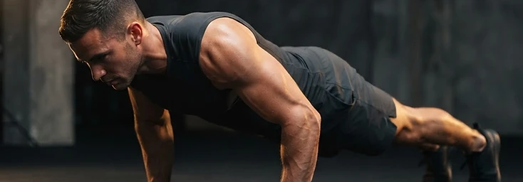 Athlete holding a strict push-up position with a straight body line on a dark floor, lit with warm gold light