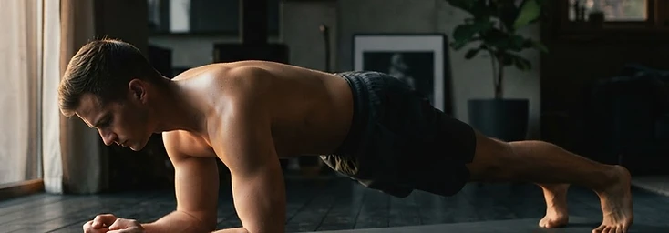 Man holding a forearm plank on a dark floor at home in soft light