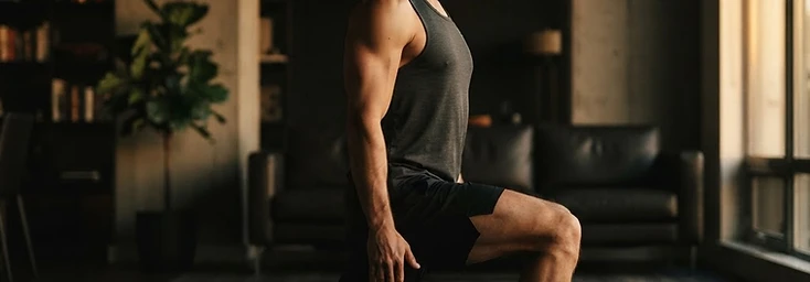 Man performing a reverse lunge with an upright torso in a dark apartment