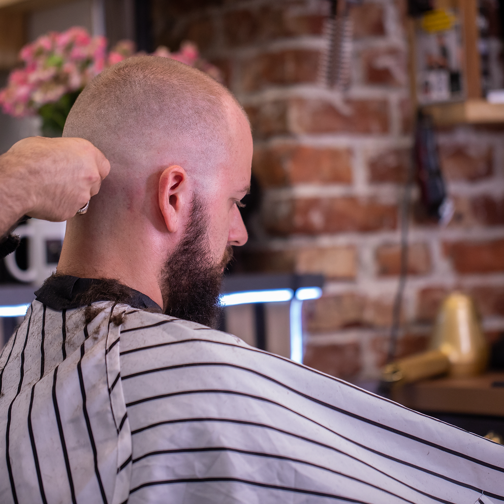 Barber at work with a customer in the chair and the shop’s brick wall in the background
