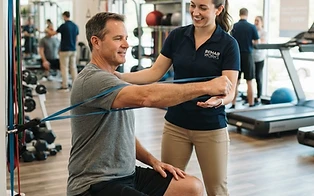A rehab specialist guiding a patient through a resistance band exercise in the clinic gym
