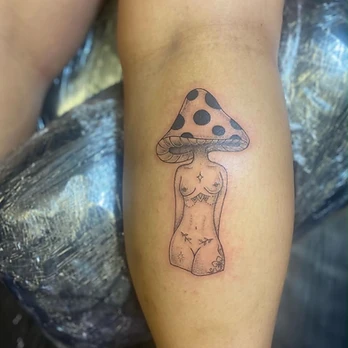 Fine line tattoo of a feminine figure with a large spotted mushroom cap for a head, a four-pointed sparkle on the sternum and small floral and geometric details down the abdomen, on a thigh
