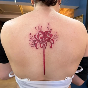 Minimalist red ink tattoo of a single red spider lily with curled petals and long sweeping stamens on a straight stem, on an upper back