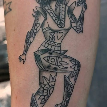 Black and grey tattoo of a space pin-up girl in a bubble helmet holding a ray gun, her suit patterned with hearts and florals, on a forearm