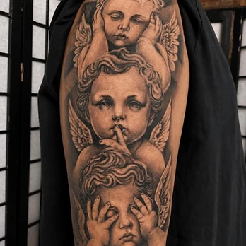 Black and grey realism tattoo of three cherubs, one with closed eyes, one shushing and one covering its eyes, on an upper arm