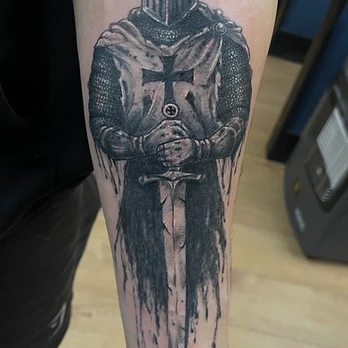 Black and grey tattoo of a medieval knight in armour and chainmail holding a longsword, with an ink-wash finish, on a forearm