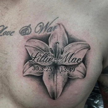 Black and grey memorial tattoo of a single lily with fine stippled shading, lettered Love & War above and the name Lillie-Mae with a date and time inside the petals, on a chest