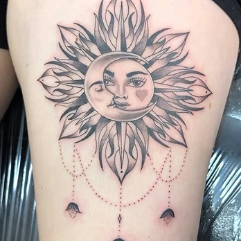 Fine-line black and grey tattoo of a crescent moon and a sun sharing one face, framed by long pointed rays with dangling beaded leaves below, on an upper thigh
