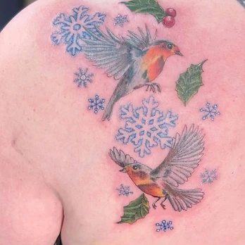 Illustrative colour tattoo of two robins in flight through falling blue snowflakes, with sprigs of green holly and red berries above and below