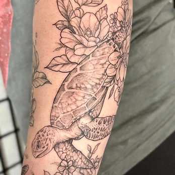 Fine-line black and grey tattoo of a sea turtle with stippled shell shading, surrounded by open flowers and leaves, on a forearm