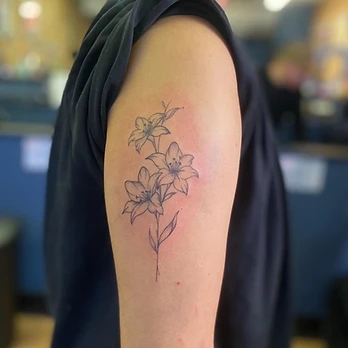 Fine line tattoo of three lily flowers opening on a single stem with leaves and light dotwork shading in the petals, on an upper arm