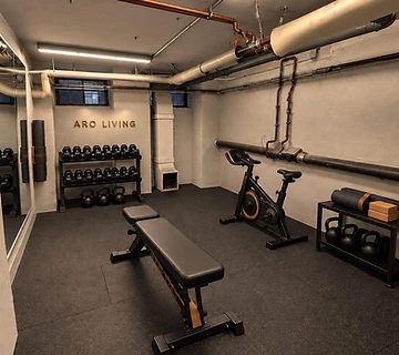 Fitness room with dumbbells, bench and exercise bike at ARO Living Berlin