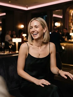 Adult woman with a blonde bob laughing in a hotel lobby bar with warm lighting