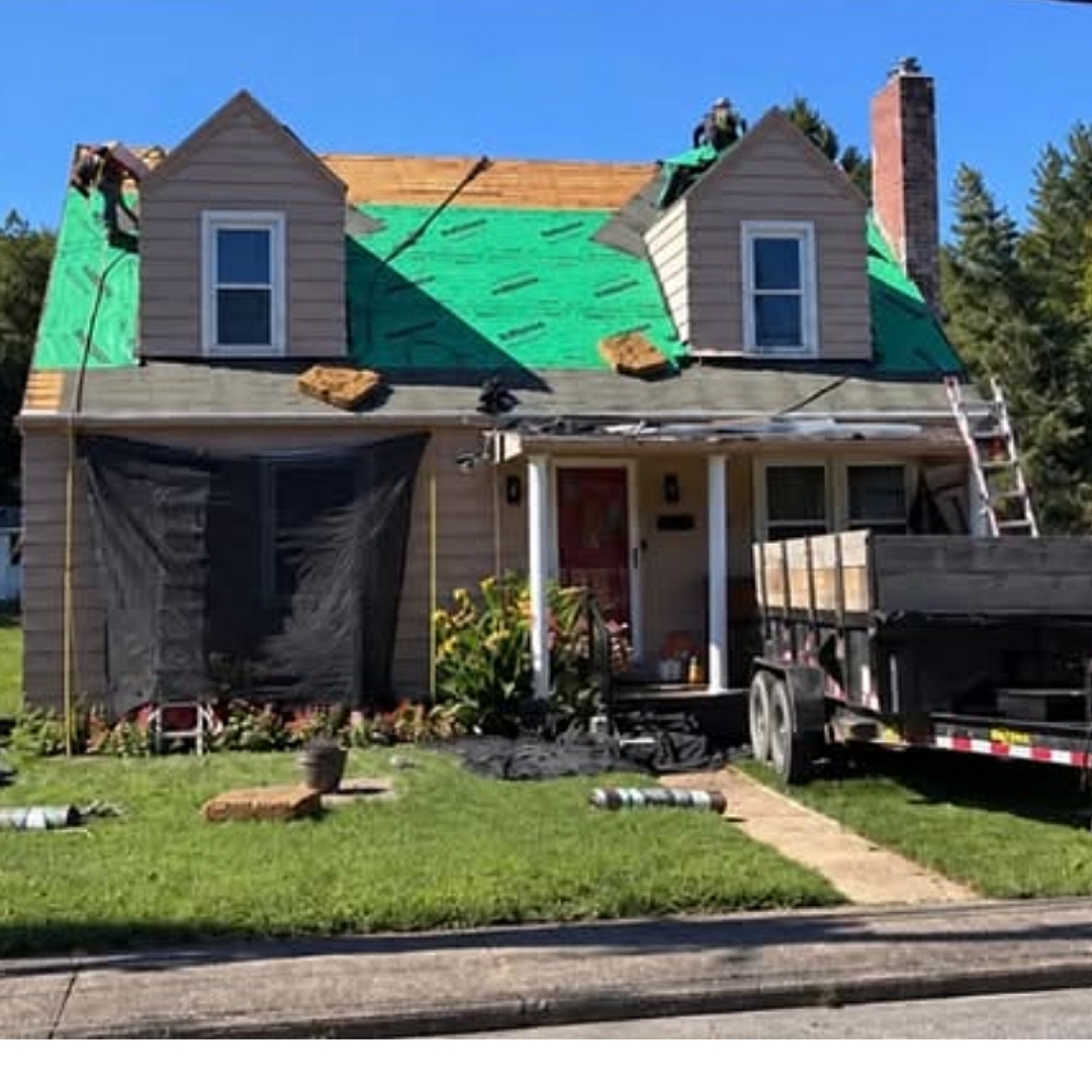 Full roof replacement in progress with green underlayment and dump trailer