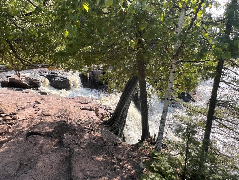 A river spilling over red rock beneath birch and cedar trees