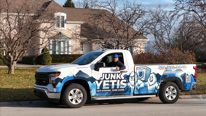 Junk Yetis branded pickup truck with blue Yeti wrap and a team member outside a Wisconsin home