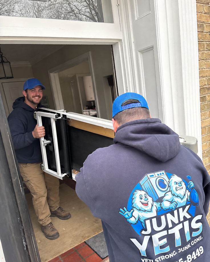 Two smiling Junk Yetis crew members carrying a glass panel through a customer's front door on moving day