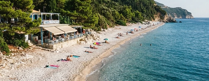 The long pebble beach at Milia on the west coast of Skopelos, with pines behind and a taverna at one end.