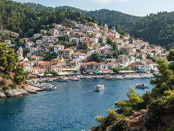 The pine-covered island town of Poros seen across the narrow strait, boats moored along the quay.