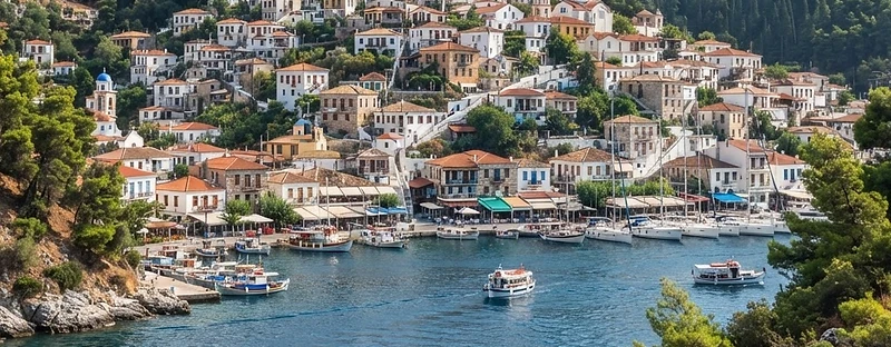 The pine-covered island town of Poros seen across the narrow strait, boats moored along the quay.