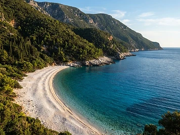 The white pebble beach at Antisamos on Kefalonia with pine-covered slopes behind it.