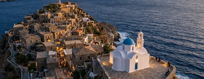 Grey stone houses with red roofs in the lanes of Afytos, with a paved terrace above the sea in the evening light.