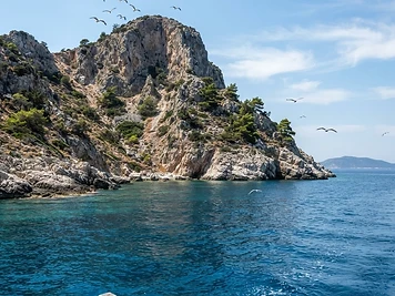 A bare rocky islet in the Alonissos marine park seen from a boat, cliffs and clear blue water.