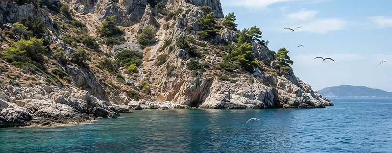 A bare rocky islet in the Alonissos marine park seen from a boat, cliffs and clear blue water.