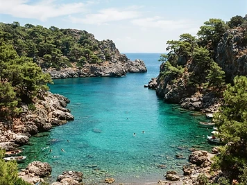 A sheltered green-blue cove enclosed by pine-covered rock at Anthony Quinn Bay, Rhodes.