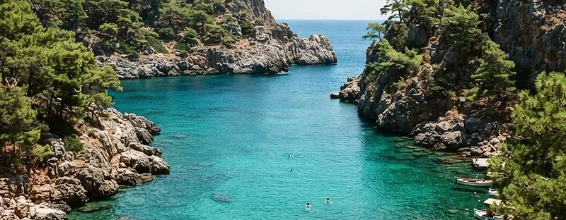 A sheltered green-blue cove enclosed by pine-covered rock at Anthony Quinn Bay, Rhodes.