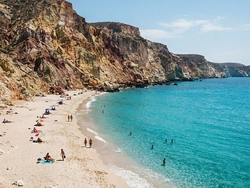 Pale sand beneath towering coloured volcanic cliffs at Firiplaka beach, Milos.