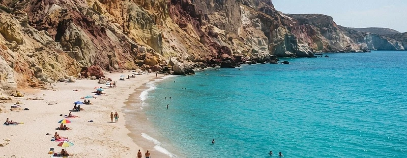 Pale sand beneath towering coloured volcanic cliffs at Firiplaka beach, Milos.