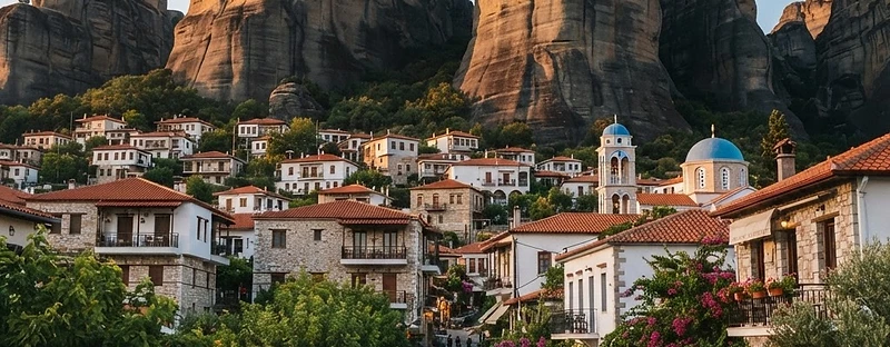 The village of Kastraki at the foot of the vertical rock pillars of Meteora, houses below the cliffs in evening light.