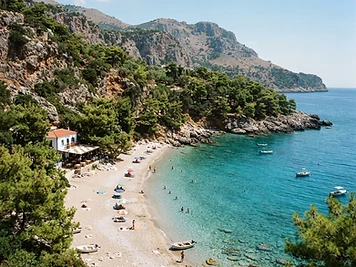 The bay at Apella on Karpathos, pale sand and pebbles with pine trees coming down to clear turquoise water.